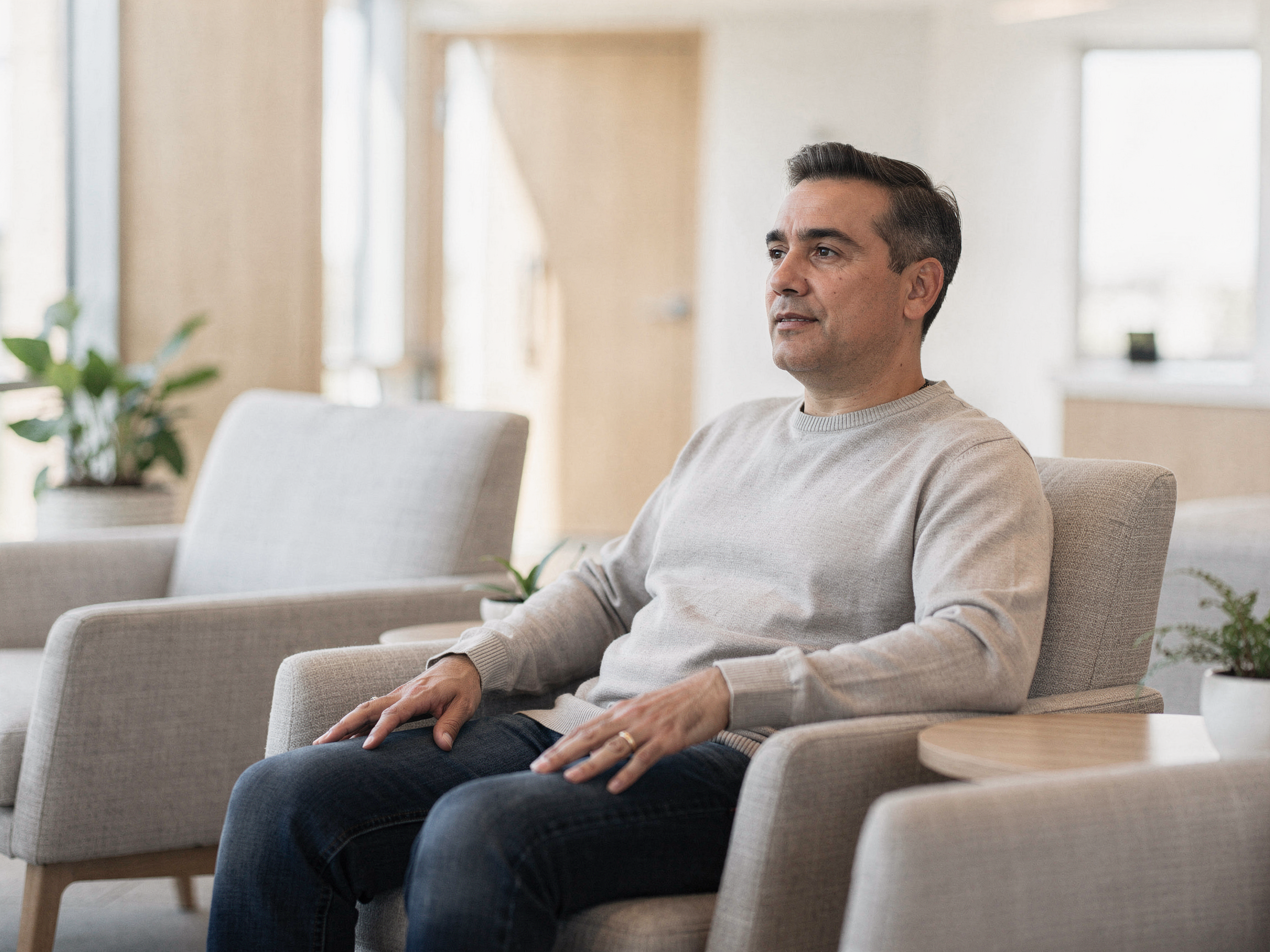 Man sitting on a couch in a light-filled clinical waiting room with plants